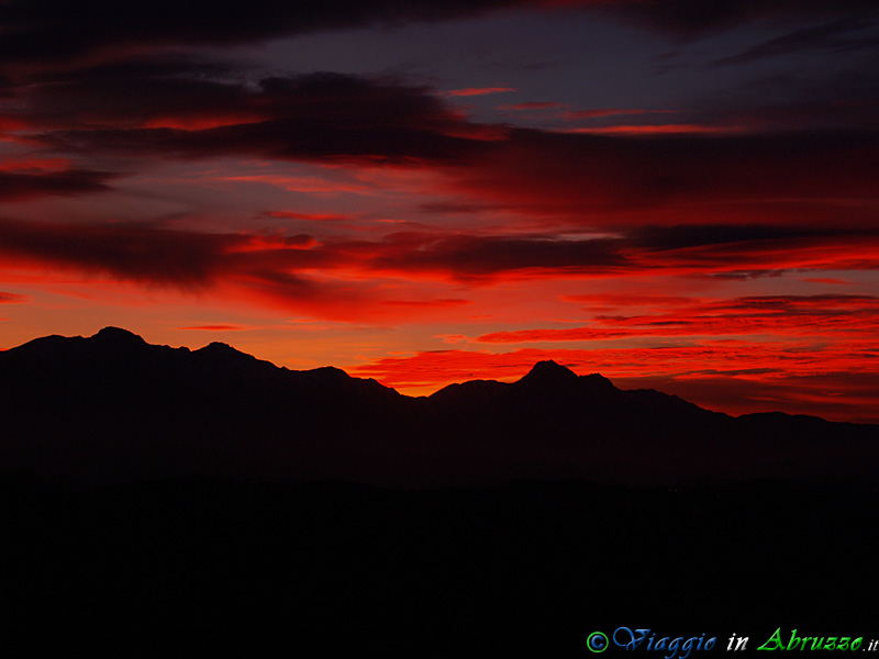 28-PB113707+.jpg - 28-PB113707+.jpg - Un infuocato tramonto sul Gran Sasso d'Italia (2.912 m.). La montagna, la più alta dell'intera catena appenninica, fu soprannominata fin dall'antichità "il Gigante che dorme" perchè, come evidenzia la parte centrale della foto, guardandola da alcune zone del teramano essa assomiglia ad una gigantesca figura umana distesa in placido sonno, con il corpo rivolto a sud.